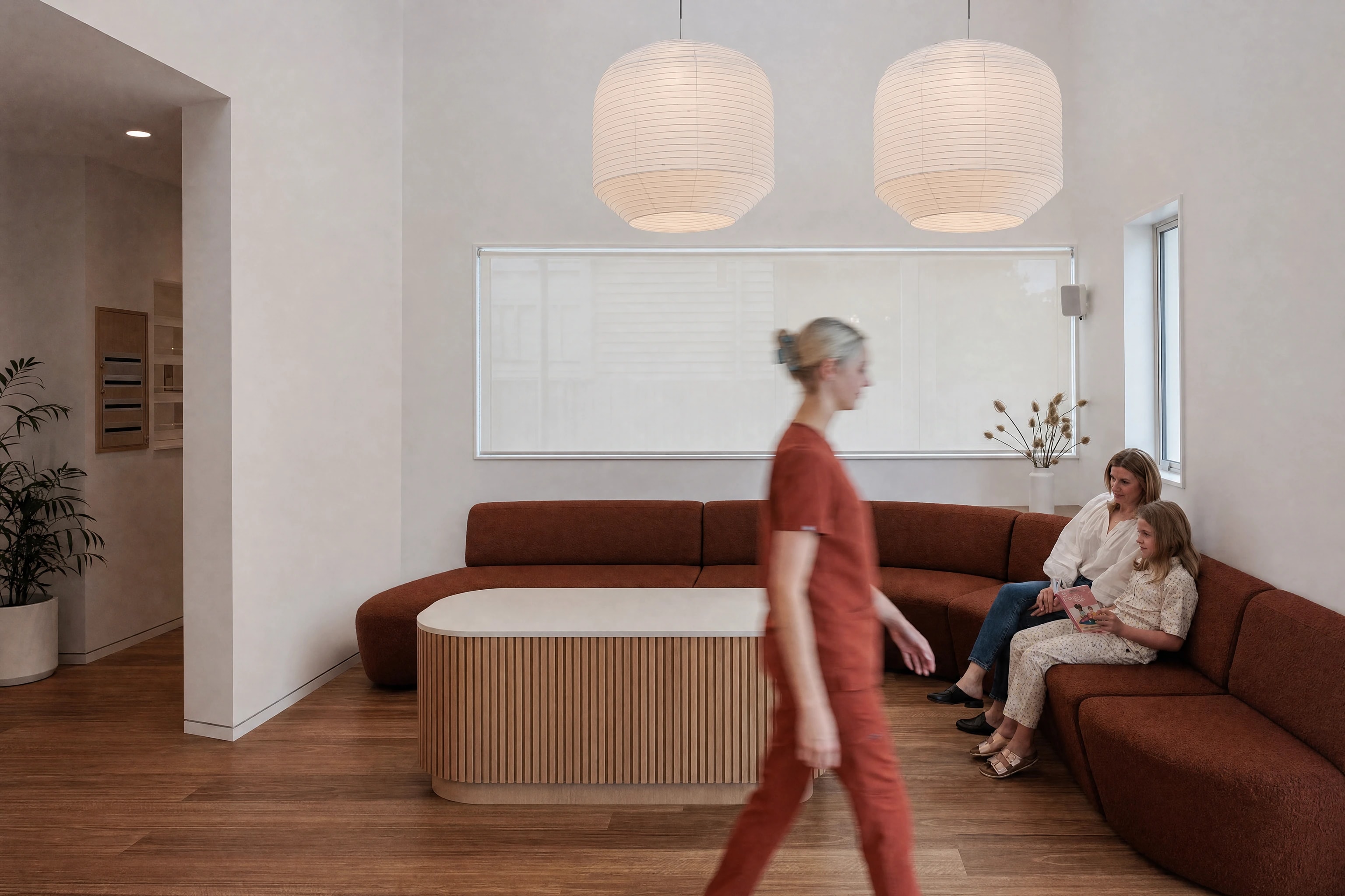 A calm clinic waiting room with a curved sofa as a staff member walks past