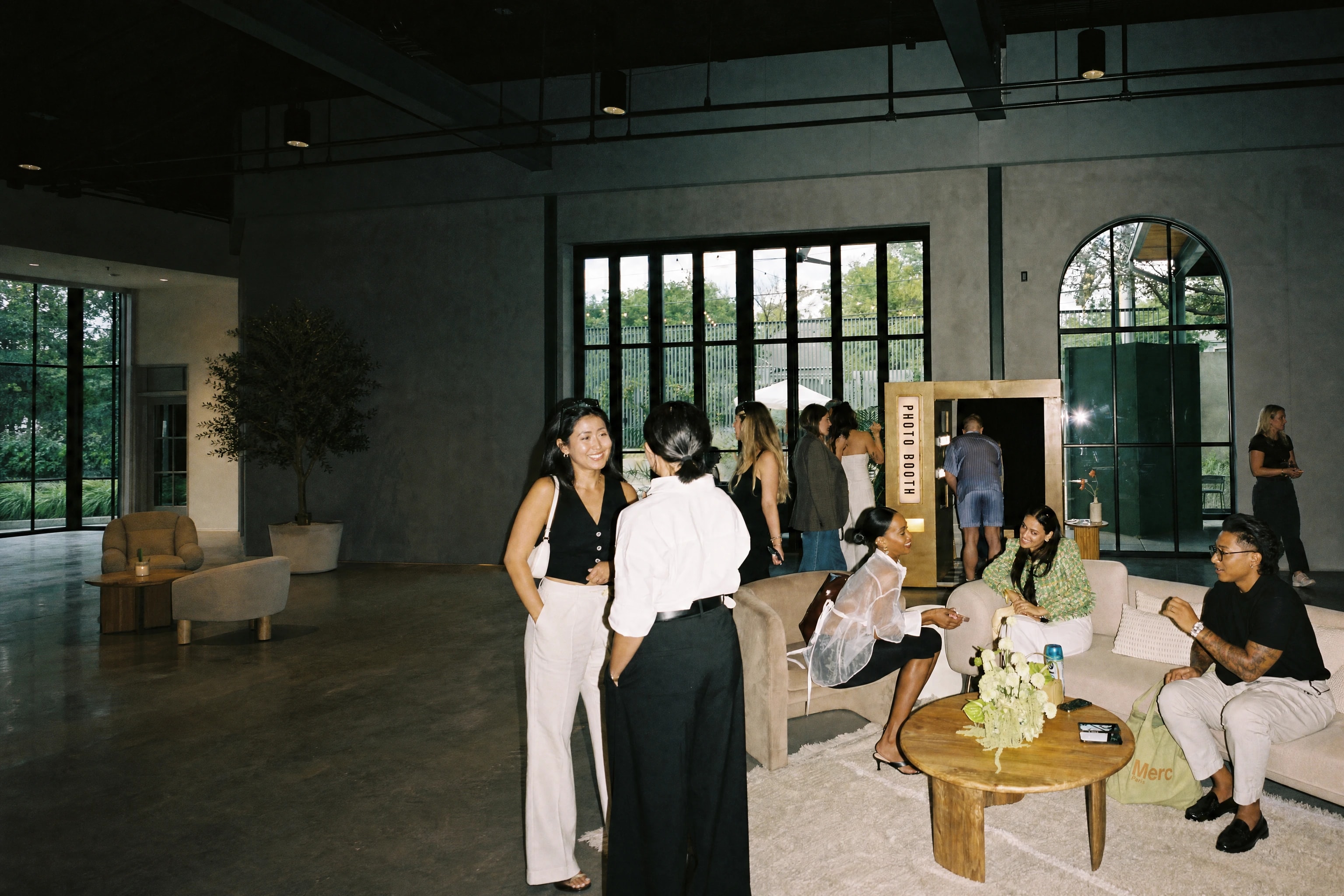 Guests mingling on sofas at a bright event venue with a photo booth