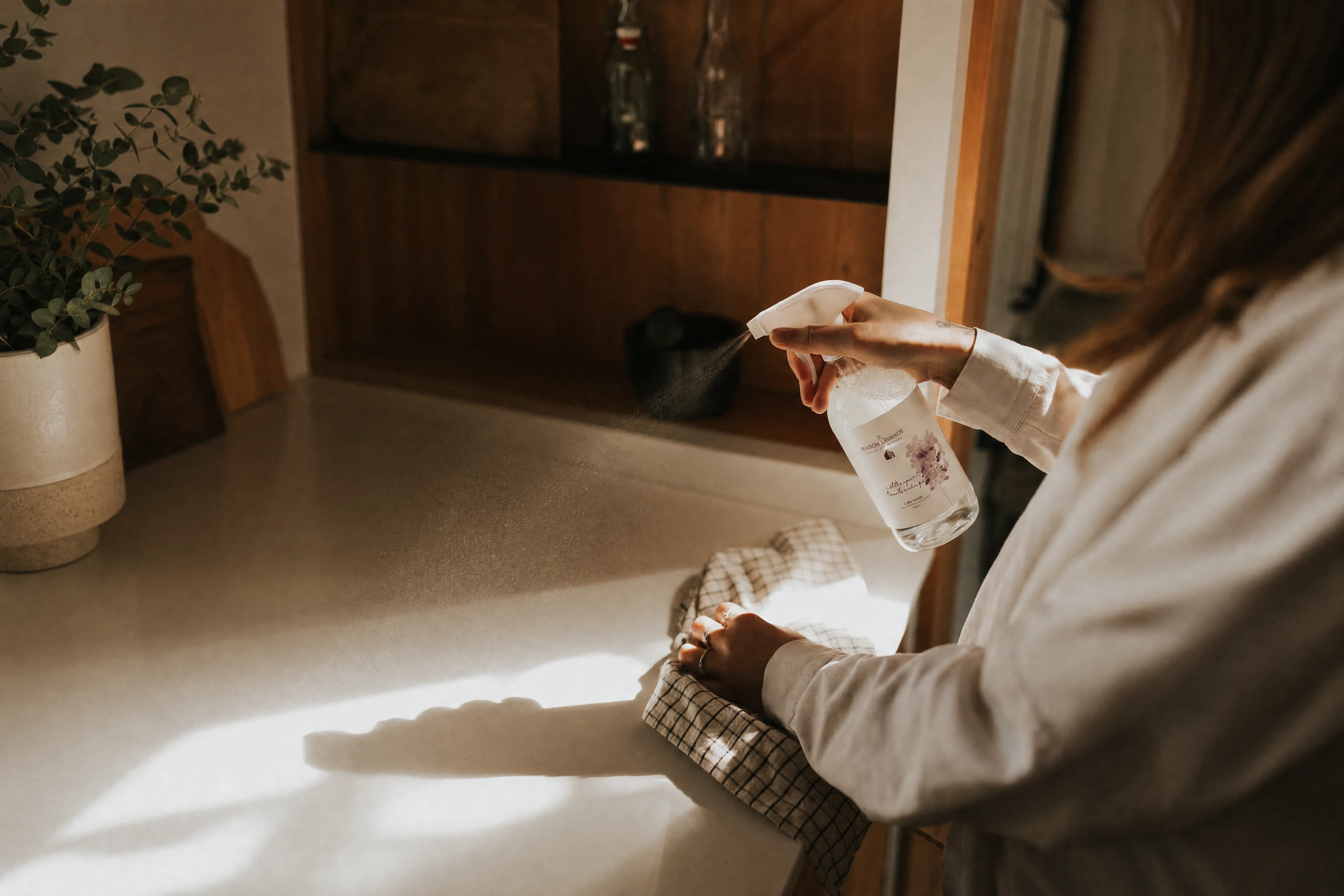 Hands spraying and wiping a kitchen counter in warm morning light