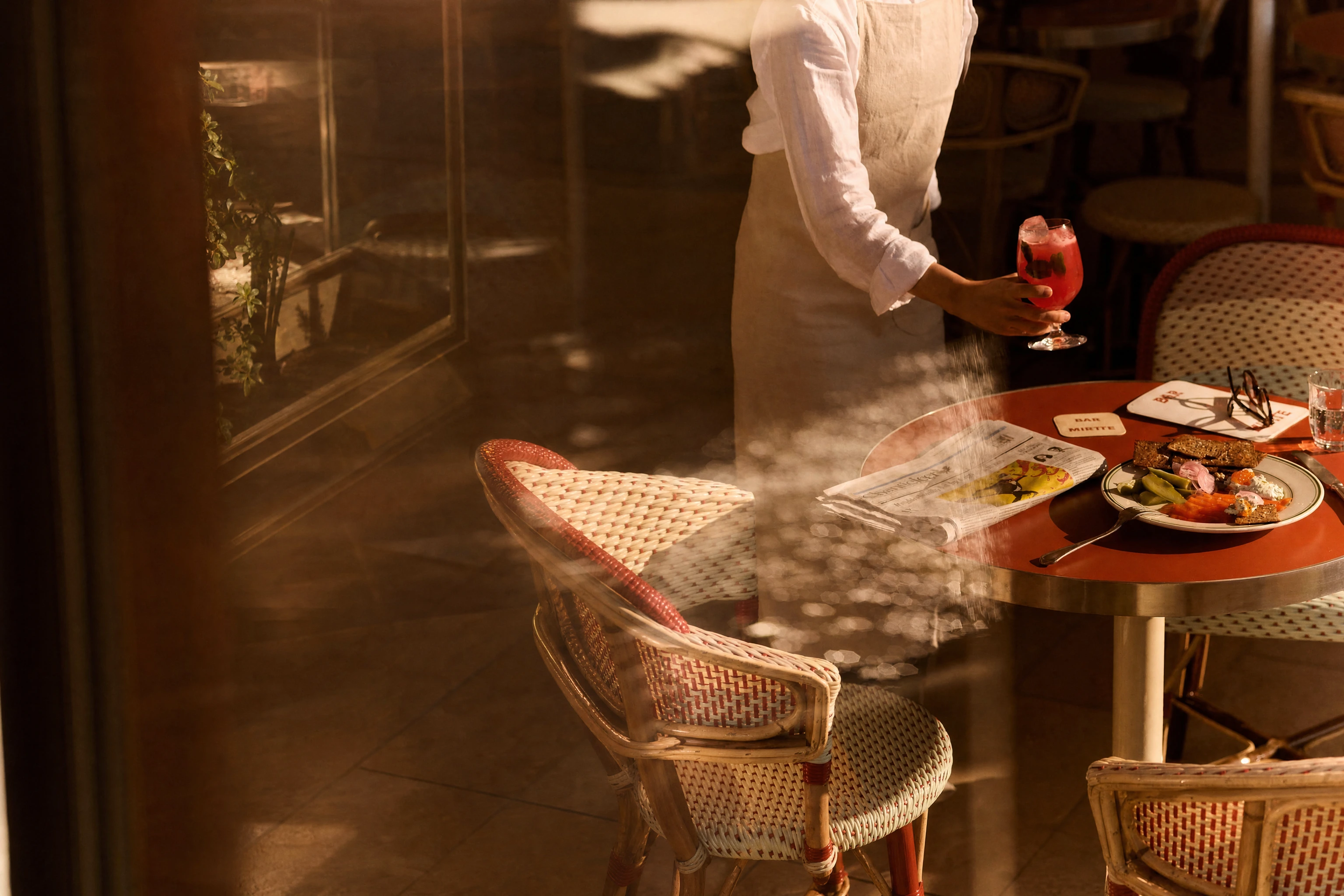 A server bringing a drink to a cafe table set with lunch