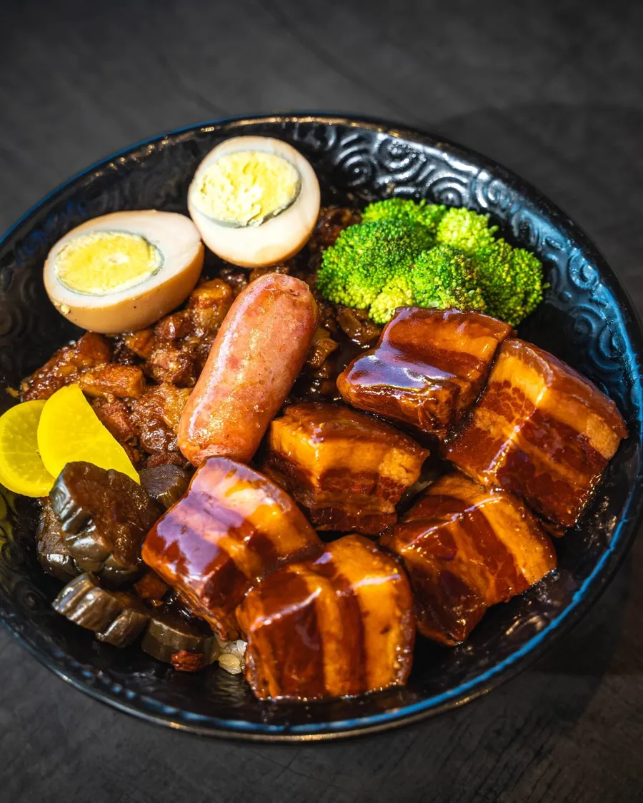 Braised pork belly, soft egg and greens in a dark bowl