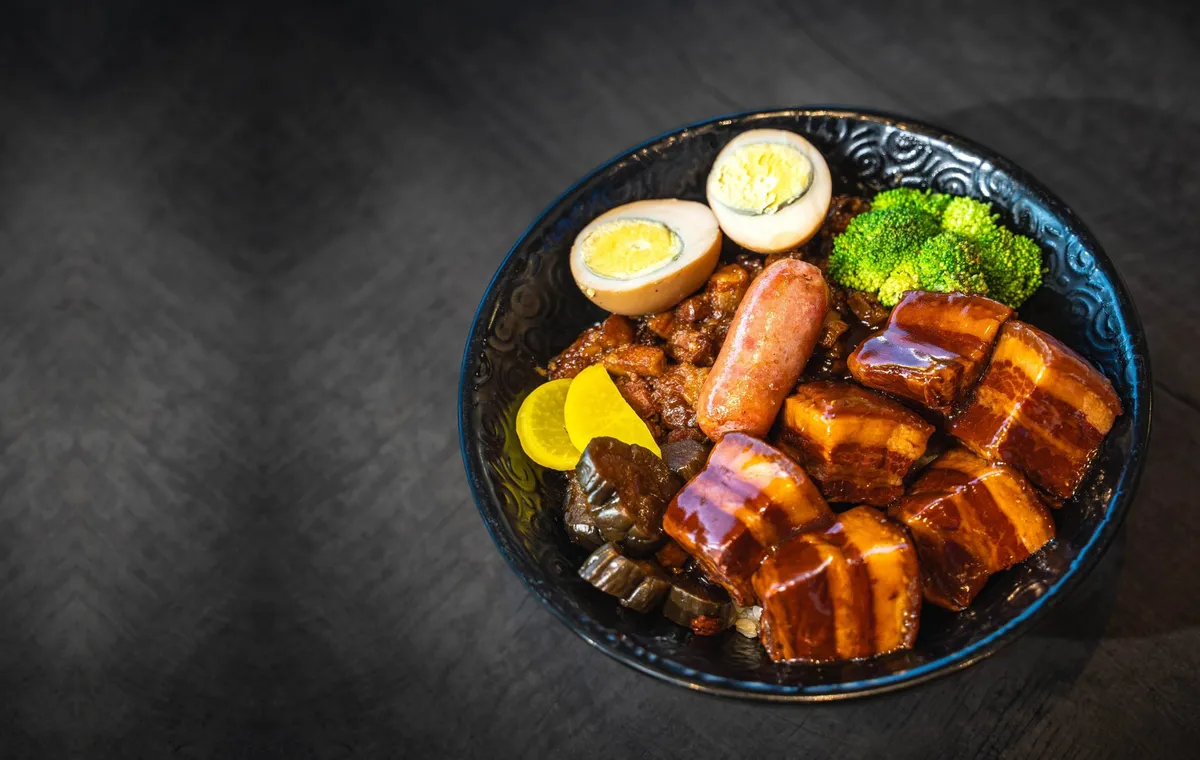 Braised pork belly, soft egg and greens in a dark bowl